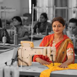 Indian women group working on sewing machine at textile factory.